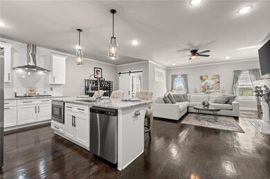 Kitchen featuring a barn door, wall chimney exhaust hood, a kitchen bar, crown molding, and dark wood-style floors