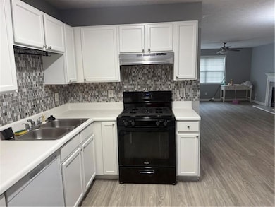 Kitchen with black range oven, white cabinetry, decorative backsplash, and light countertops