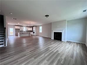 Unfurnished living room with dark wood-style floors, stairs, and a fireplace