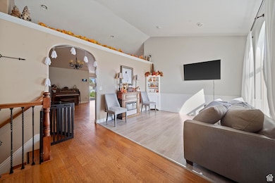 Living area with arched walkways, wood finished floors, high vaulted ceiling, and a chandelier