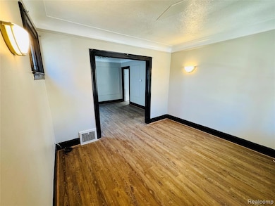 Unfurnished room with light wood-style floors, a textured ceiling, and ornamental molding