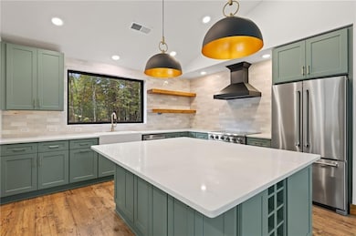 Kitchen with green cabinetry, stainless steel appliances, open shelves, recessed lighting, and light wood-style floors