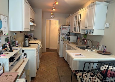 Kitchen featuring glass insert cabinets, light countertops, white cabinets, dark tile patterned floors, and white appliances