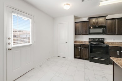 Kitchen featuring dark brown cabinets, black appliances, light marble finish floors, and light stone countertops