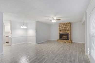 Unfurnished living room featuring wood finish floors, ceiling fan, a brick fireplace, a chandelier, and a textured ceiling