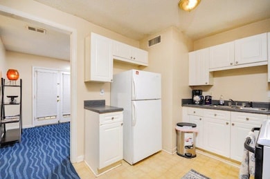 Kitchen featuring dark countertops, freestanding refrigerator, range, white cabinets, and a textured ceiling