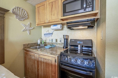 Kitchen with black microwave, sink, a textured cei