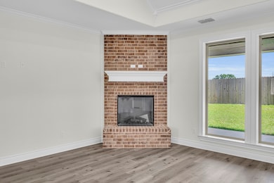 Unfurnished living room with ornamental molding, wood finished floors, and a brick fireplace