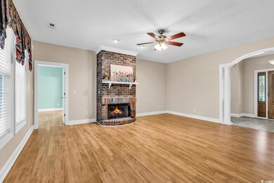 Unfurnished living room with arched walkways, a brick fireplace, ceiling fan, and light wood-type flooring