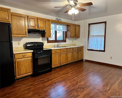 Kitchen with black appliances, light countertops, brown cabinets, and dark wood-type flooring