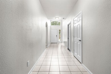 Hall featuring a textured wall, light tile patterned floors, and arched walkways