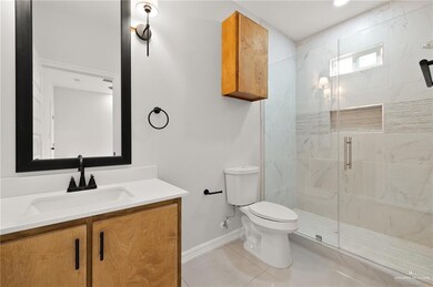 Bathroom featuring tile patterned flooring, toilet, vanity, baseboards, and a marble finish shower