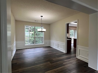 Unfurnished dining area featuring plenty of natural light, a decorative wall, a chandelier, wainscoting, and dark wood finished floors