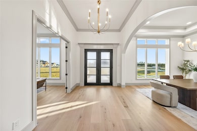 Foyer entrance with a chandelier, light wood-style flooring, plenty of natural light, arched walkways, and ornamental molding