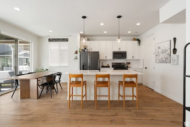 Kitchen with tasteful backsplash, pendant lighting, white cabinets, stainless steel appliances, and light wood finished floors
