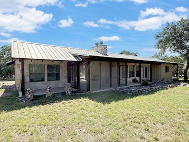 Rear view of house featuring a chimney, a standing seam roof, a metal roof, and a lawn