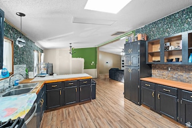 Kitchen with wallpapered walls, a peninsula, decorative light fixtures, open shelves, and open floor plan