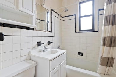 Bathroom featuring vanity, shower / bathtub combination with curtain, toilet, and tile walls