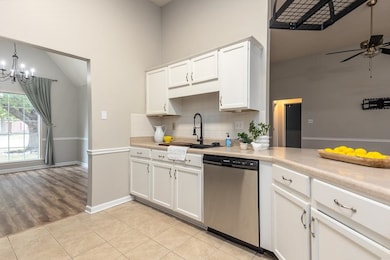 Kitchen featuring light tile patterned floors, white cabinets, stainless steel dishwasher, light countertops, and backsplash