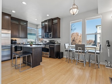 Kitchen featuring dark brown cabinetry, a breakfast bar, glass insert cabinets, stainless steel appliances, and recessed lighting