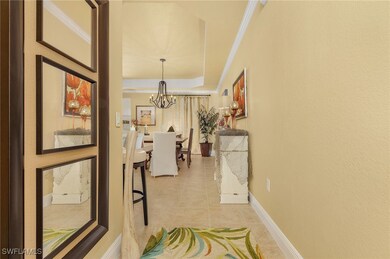 Hall with a notable chandelier, light tile patterned floors, baseboards, crown molding, and a raised ceiling
