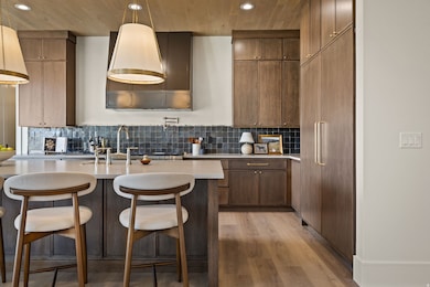 Kitchen featuring light wood-style flooring, a breakfast bar, decorative backsplash, pendant lighting, and paneled refrigerator