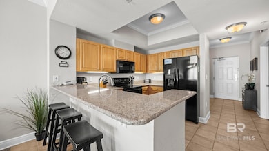 Kitchen with crown molding, a peninsula, black appliances, light tile patterned floors, and a kitchen bar