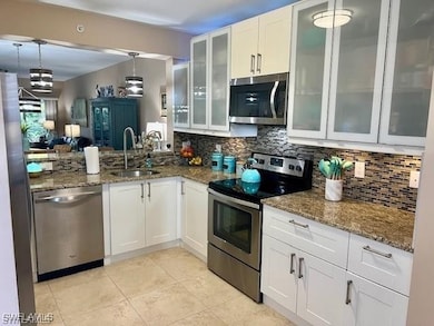 Kitchen with white cabinetry, appliances with stainless steel finishes, and dark stone counters