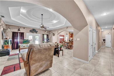 Living area with light tile patterned floors, baseboards, arched walkways, ceiling fan, and a raised ceiling