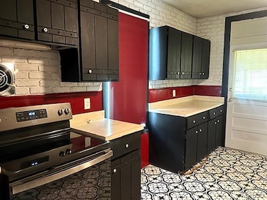Kitchen featuring stainless steel range with electric stovetop, dark cabinets, and light countertops