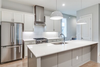 Kitchen with stainless steel appliances, backsplash, white cabinets, wall chimney range hood, and an island with sink