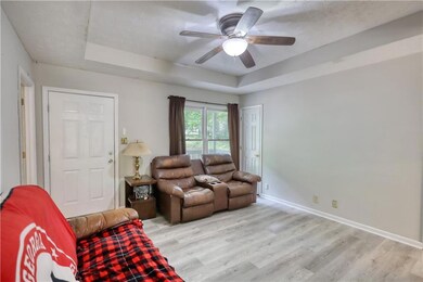Living room with a tray ceiling, light wood-style floors, a ceiling fan, and baseboards