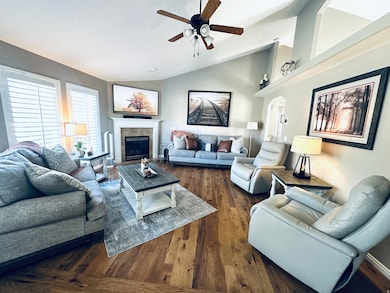 Living room featuring vaulted ceiling, dark wood-type flooring, ceiling fan, a fireplace, and arched walkways