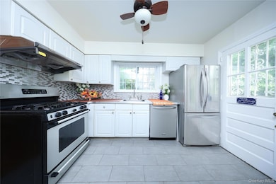 Kitchen featuring stainless steel appliances, backsplash, under cabinet range hood, a ceiling fan, and white cabinets