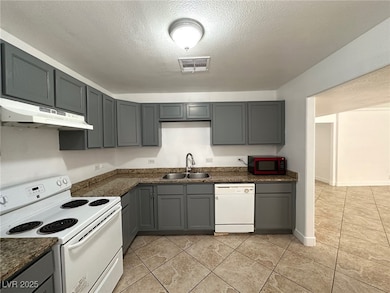 Kitchen featuring gray cabinets, white appliances, a textured ceiling, under cabinet range hood, and light tile patterned floors