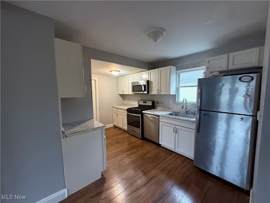 Kitchen featuring appliances with stainless steel finishes, dark wood-style flooring, white cabinets, tasteful backsplash, and light stone counters