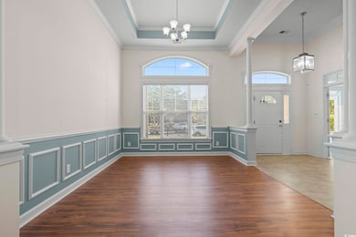 Foyer featuring decorative columns, a chandelier, crown molding, LVF, and wainscoting