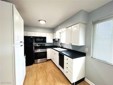 Kitchen featuring black appliances, dark countertops, white cabinets, and plenty of natural light