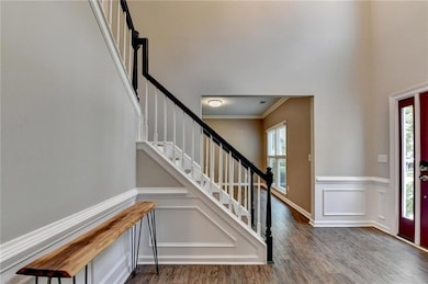 Foyer with stairway, wood finished floors, ornamental molding, a wainscoted wall, and a decorative wall