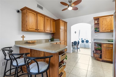 Kitchen with open shelves, arched walkways, lofted ceiling, a peninsula, and brown cabinets