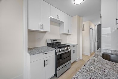 Kitchen with appliances with stainless steel finishes, light stone countertops, light wood-style floors, and white cabinetry