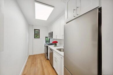 Kitchen featuring stainless steel appliances, white cabinets, light wood-style floors, and light stone counters