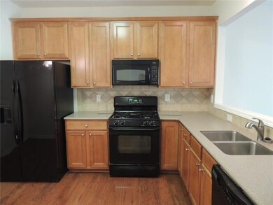 Kitchen with black appliances, a sink, dark wood-type flooring, light countertops, and backsplash