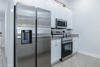 Kitchen featuring baseboards, white cabinetry, lig