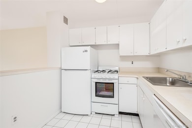 Kitchen with white appliances, white cabinetry, light countertops, and light tile patterned flooring