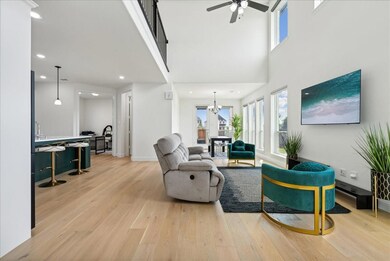 Living room with a wealth of natural light, light wood-style floors, a towering ceiling, and ceiling fan with notable chandelier