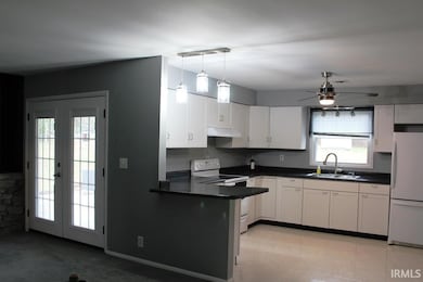 Kitchen featuring dark countertops, white appliances, a peninsula, and white cabinetry
