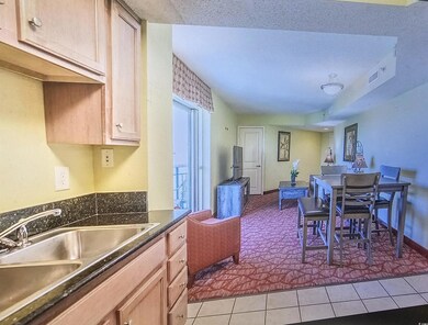 Kitchen with light brown cabinets, dark stone countertops, light tile patterned flooring, open floor plan, and light carpet