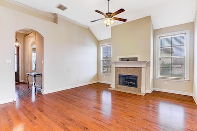 Unfurnished living room featuring light wood finished floors, arched walkways, a ceiling fan, a tile fireplace, and vaulted ceiling