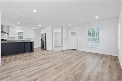 Kitchen featuring appliances with stainless steel finishes, ornamental molding, wall chimney range hood, open floor plan, and white cabinetry